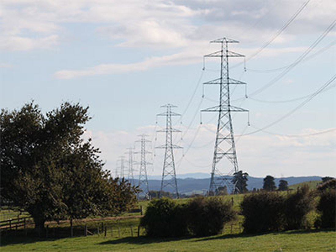 Row of power lines in a field with moonlight tower in the background