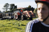 A farmer riding along a red tractor with a nearby individual