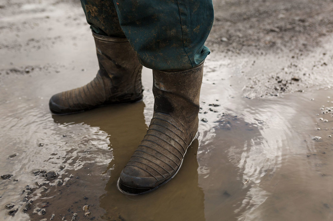A farm worker in a pair of boots standing in a muddy puddle