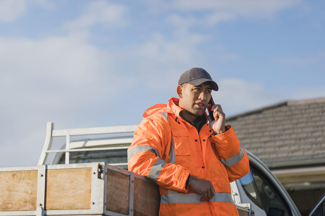 A dairy farmer making a phone call outside, leaning against his ute