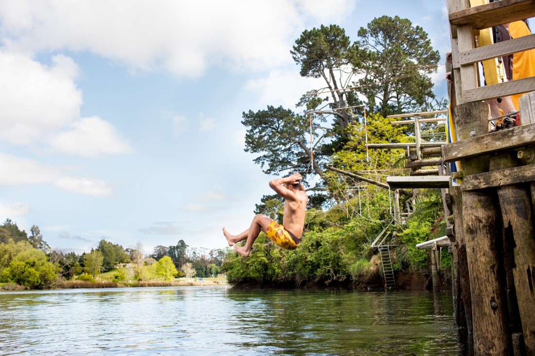 A boy having fun with his friends, jumping into a river to play and swim