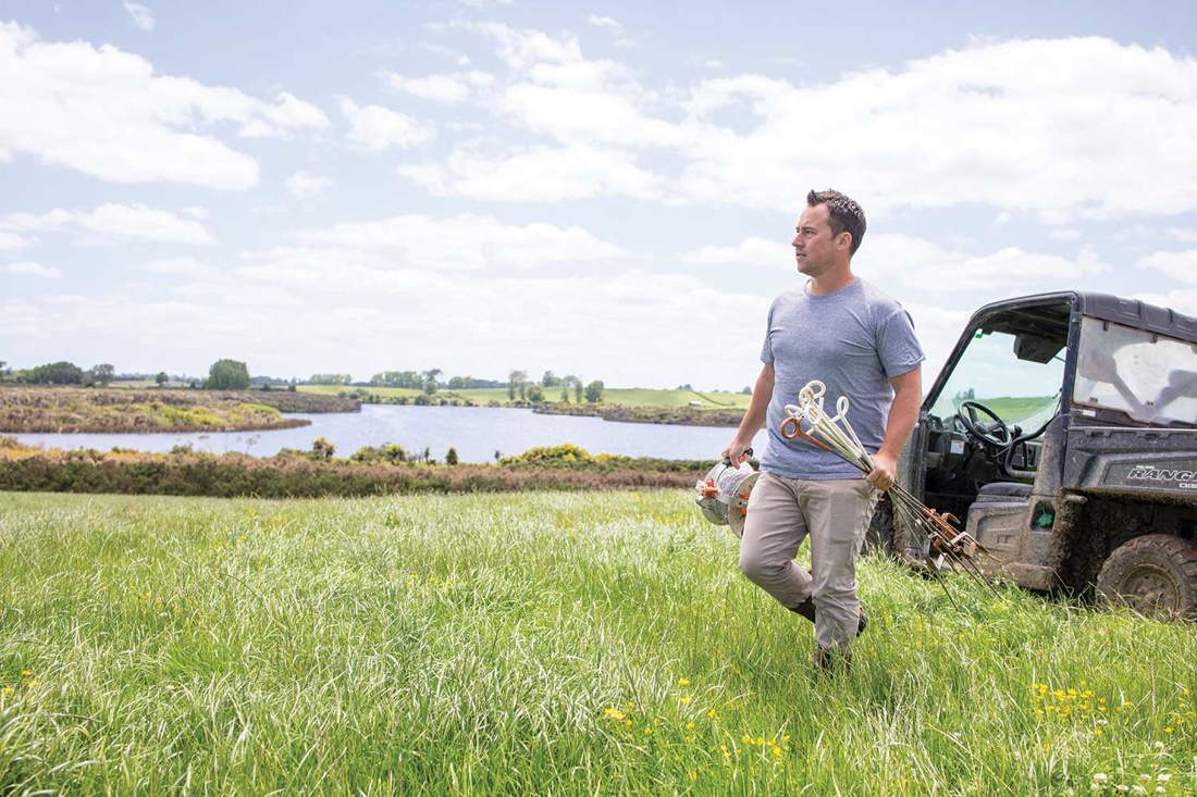 A farm owner out in a paddock near a river with fencing equipment and a 4x4