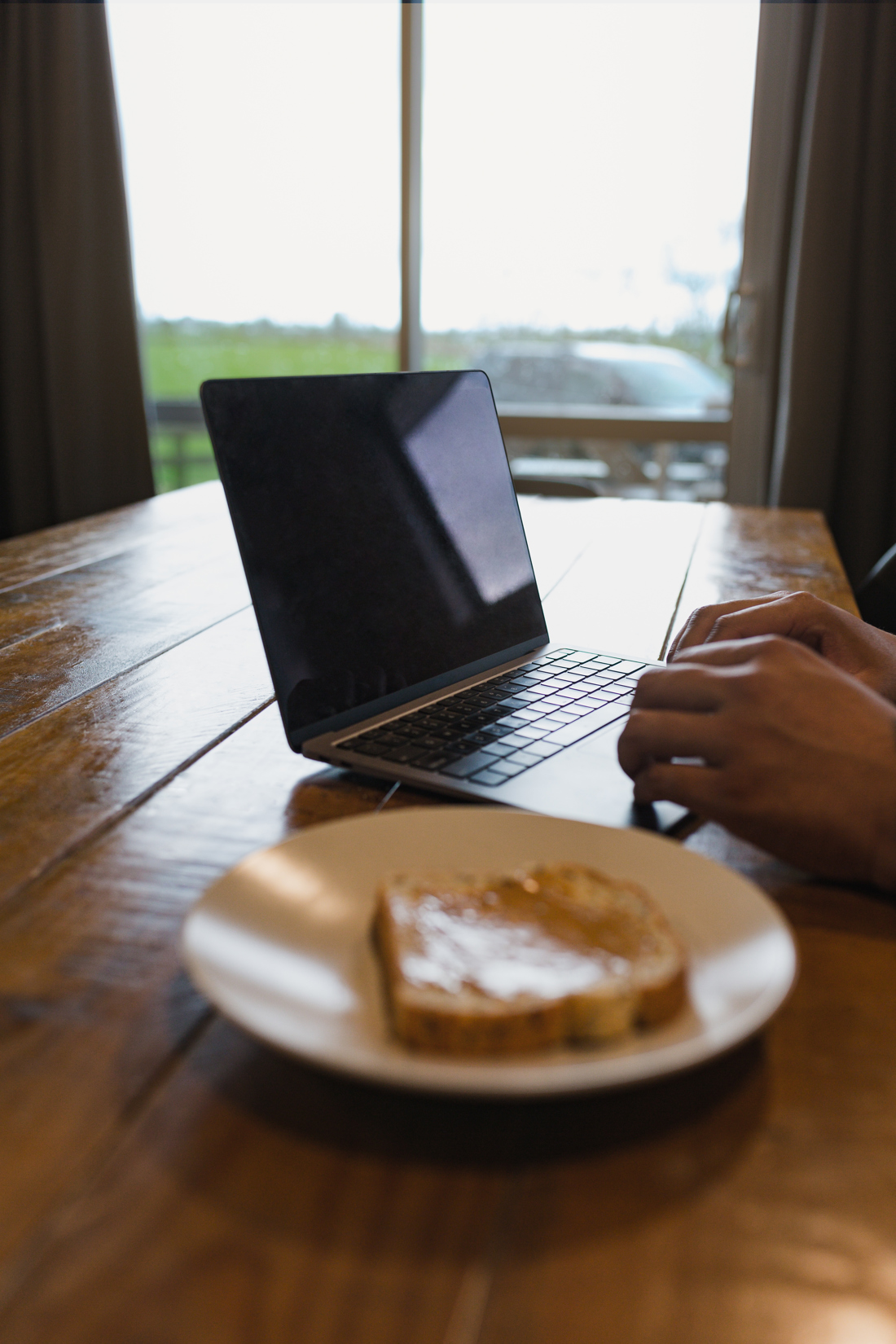A bread on a plate and a person working on his laptop
