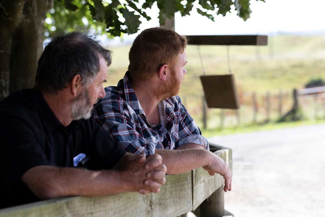 Two dairy farmers leaning on a fence and talking