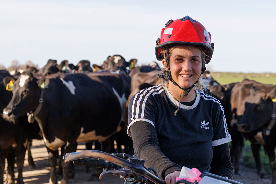 Female farm assistant on a quad bike with dairy cows in the background